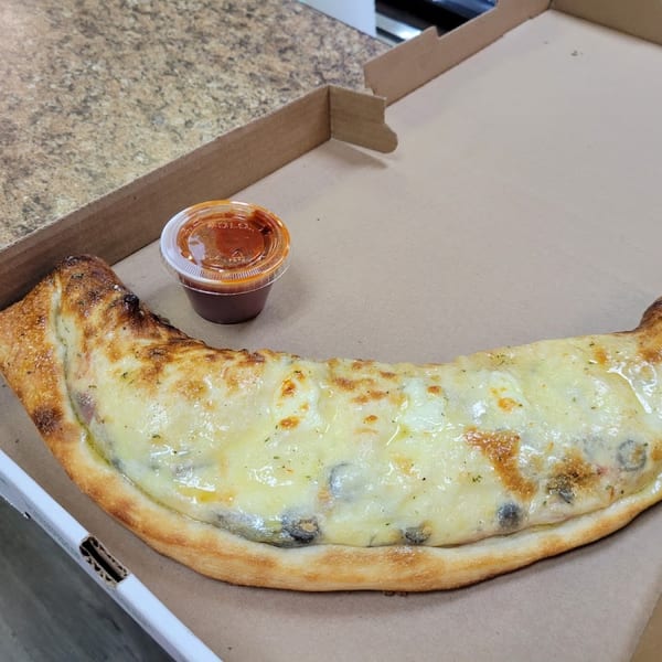 A golden-brown calzone with melted cheese and a side of marinara sauce in a pizza box.