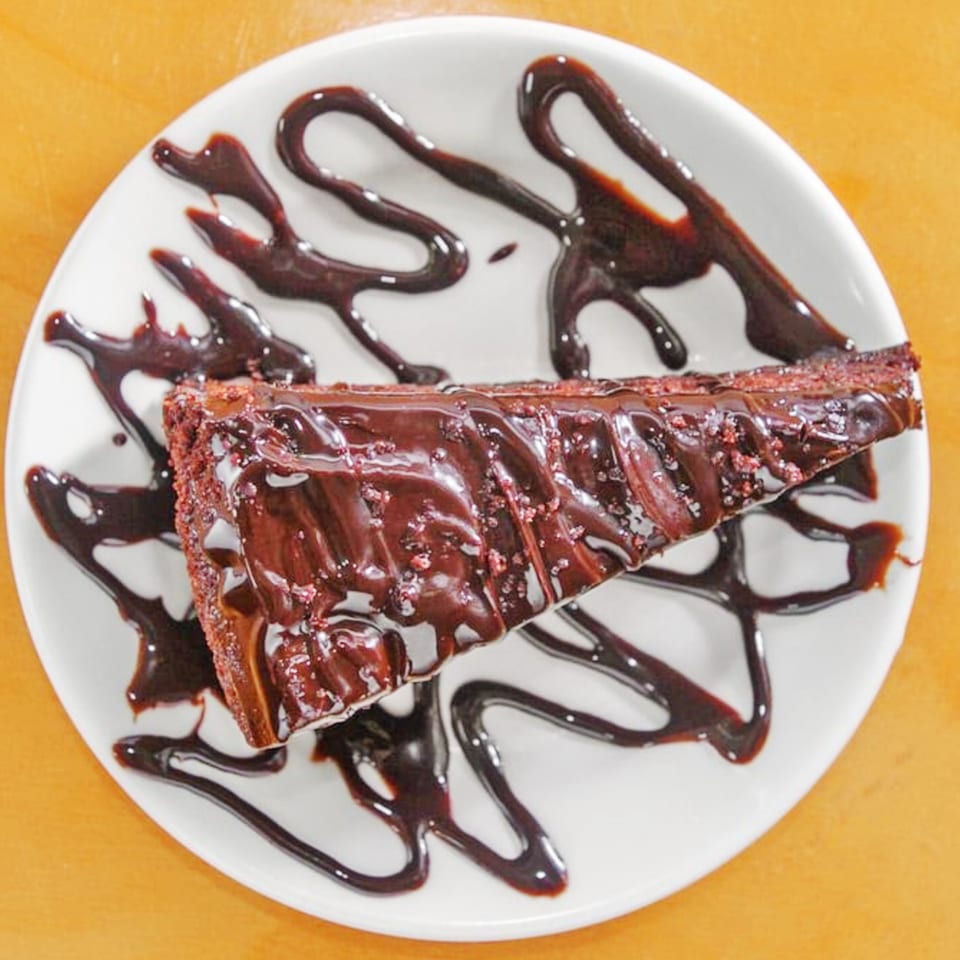 A slice of rich chocolate cake with chocolate drizzle on a white plate.