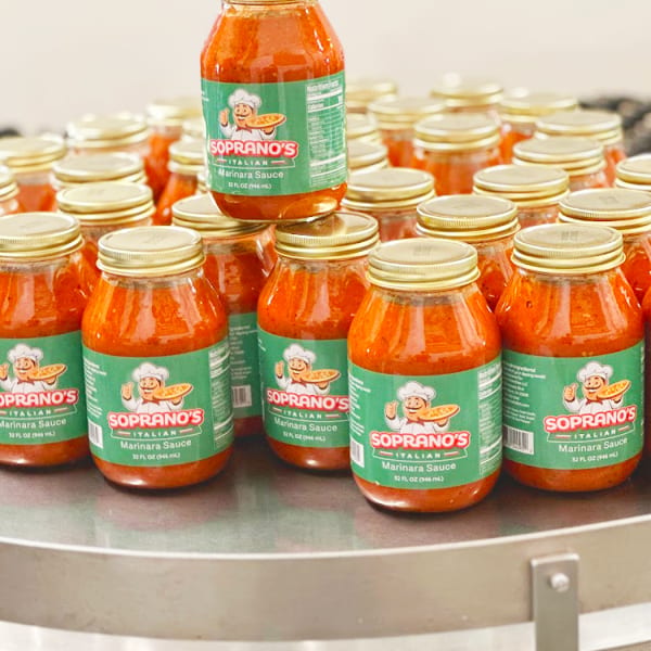 Numerous jars of Soprano's Italian Marinara Sauce with green labels, one jar stacked on top.