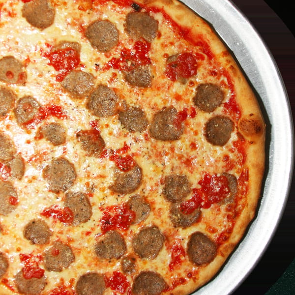 Close-up of a whole sausage pizza with melted cheese and red sauce on a metal tray.
