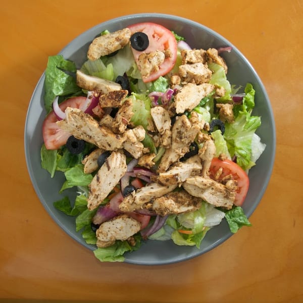 Overhead view of a salad with grilled chicken, lettuce, tomatoes, red onions, and black olives.