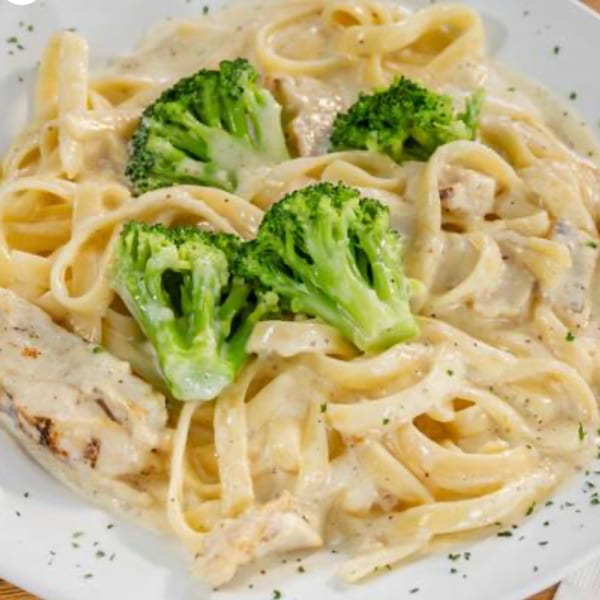 Creamy fettuccine alfredo with grilled chicken and fresh broccoli florets on a white plate.